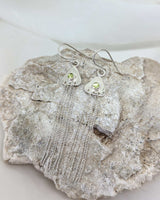 two triangular earrings on a rock with peridots in their center. there are strands of sterling silver dangling from them. 