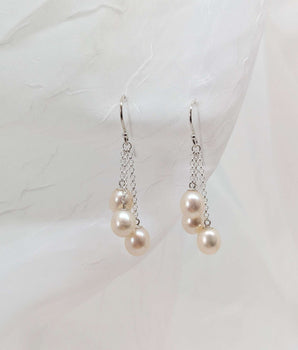 three dangling pearl earrings laid on a white background made from sterling silver. A slightly different angle.