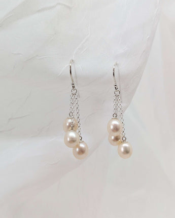 three dangling pearl earrings laid on a white background made from sterling silver. A slightly different angle.