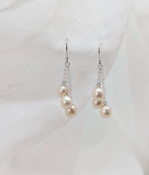 three dangling pearl earrings laid on a white background made from sterling silver.