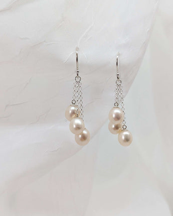 three dangling pearl earrings laid on a white background made from sterling silver.