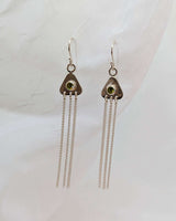 two triangular earrings on a white background with peridots in their center. there are strands of sterling silver dangling from them. 
