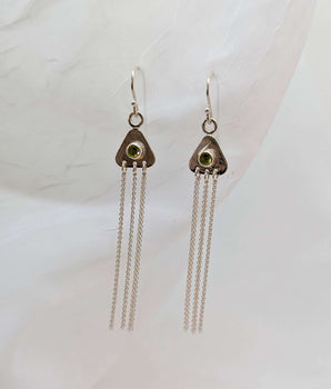 two triangular earrings on a white background with peridots in their center. there are strands of sterling silver dangling from them. 