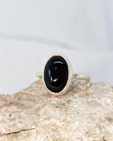 This picture shows a gorgeous sterling silver (925 silver) ring. The ring is adorned with a deep black onyx gem. The ring is presented on a white background and is shown on a rock. This image offers a close-up of the ring. 
