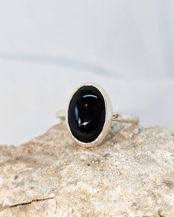 This picture shows a gorgeous sterling silver (925 silver) ring. The ring is adorned with a deep black onyx gem. The ring is presented on a white background and is shown on a rock. This image offers a close-up of the ring. 