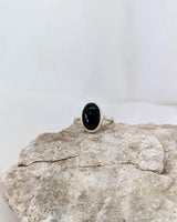 This picture shows a gorgeous sterling silver (925 silver) ring. The ring is adorned with a deep black onyx gem. The ring is presented on a white background and is shown on a rock.