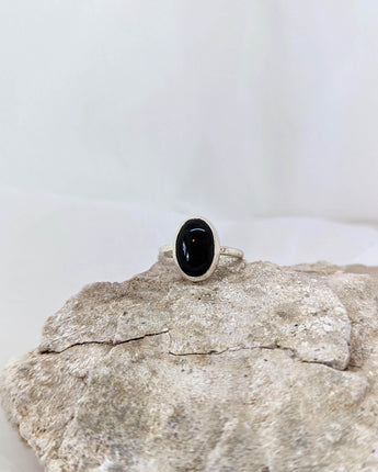 This picture shows a gorgeous sterling silver (925 silver) ring. The ring is adorned with a deep black onyx gem. The ring is presented on a white background and is shown on a rock.