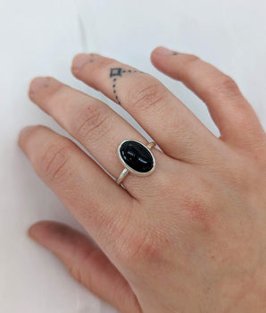 This picture shows a gorgeous sterling silver (925 silver) ring. The ring is adorned with a deep black onyx gem. The ring is presented on a white background and is on my middle finger. My tattoo on my ring finger is showing. 