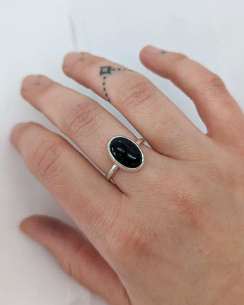 This picture shows a gorgeous sterling silver (925 silver) ring. The ring is adorned with a deep black onyx gem. The ring is presented on a white background and is on my middle finger. My tattoo on my ring finger is showing. 