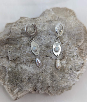 This picture shows a gorgeous sterling silver (925 silver) earrings. The earrings have dangling eye shaped pendants with an opal in their center and a pearl dangling beneath them. The earrings are presented on a white background and is shown on a rock.