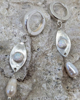 This picture shows a gorgeous sterling silver (925 silver) earrings. The earrings have dangling eye shaped pendants with an opal in their center and a pearl dangling beneath them. The earrings are presented on a rock. This picture offers a closeup image of the earrings.