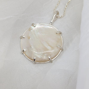 Round mother of peal necklace with sterling silver chain. It is laid on a white background.