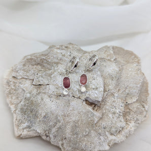 a pair of pink tourmaline earrings with white moonstones laying on a stone and a white background. 