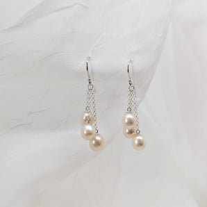 three dangling pearl earrings laid on a white background made from sterling silver. A slightly different angle.