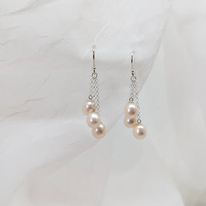 three dangling pearl earrings laid on a white background made from sterling silver.
