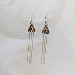 two triangular earrings on a white background with peridots in their center. there are strands of sterling silver dangling from them. 