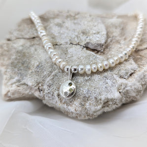 pearl necklace and sterling silver pendant on a stone and a white background. 