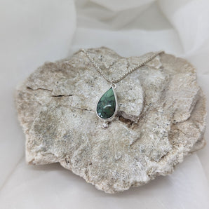 teardrop shaped turquoise pendant, one cubic zirconium, on a rock with a white background. 