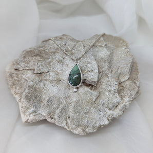 teardrop shaped turquoise pendant, one cubic zirconium, on a rock with a white background.  different angle