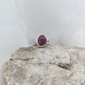 ruby ring with two white moonstones on each side. Laying on a rock and a white background. 